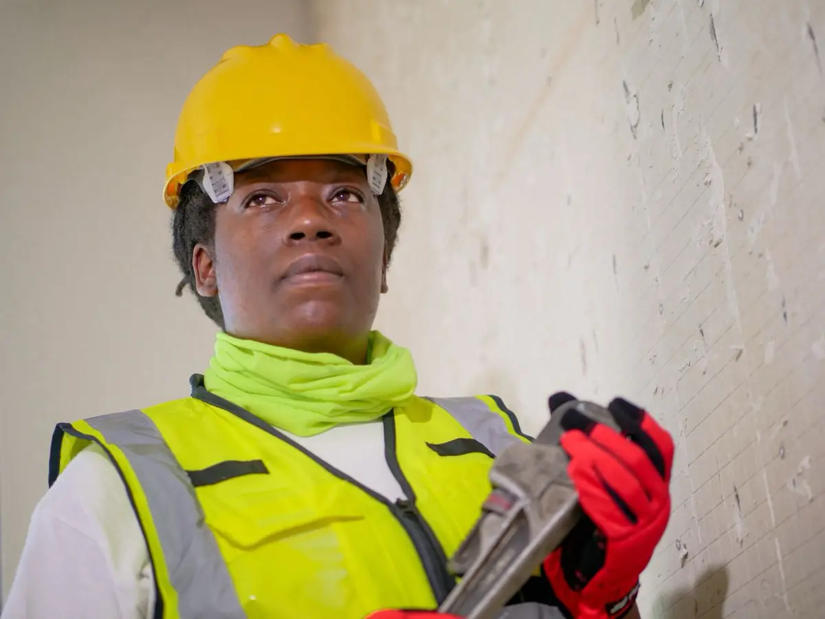 A worker in a hard hat and high visibility vest holding a pipe wrench